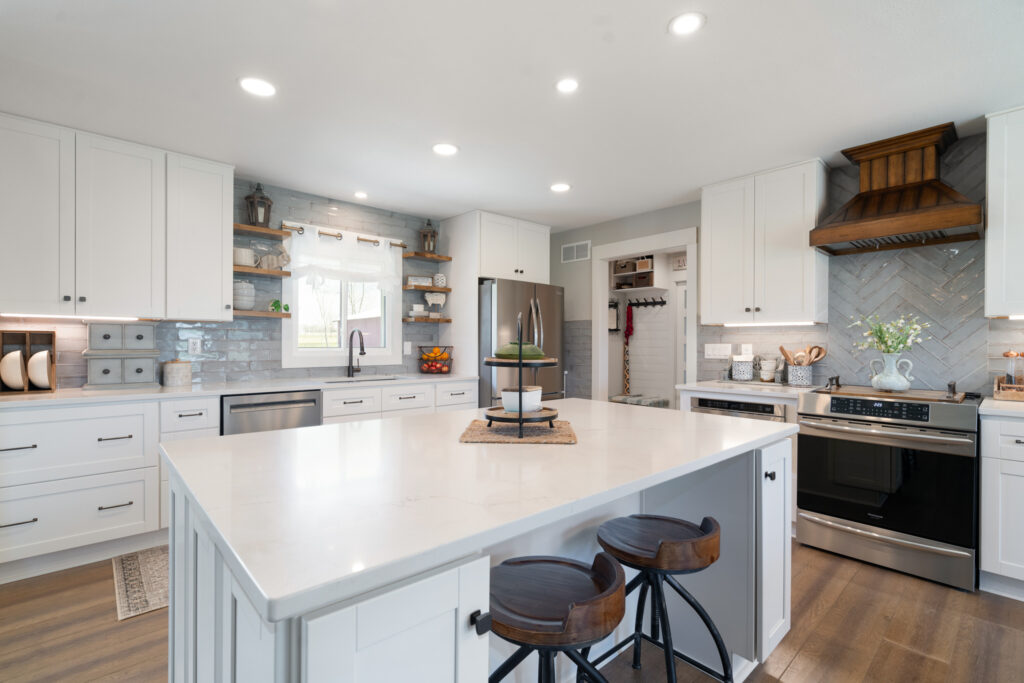 White kitchen island with white cabinets, white countertop, two bar stools, and stainless steel appliances.