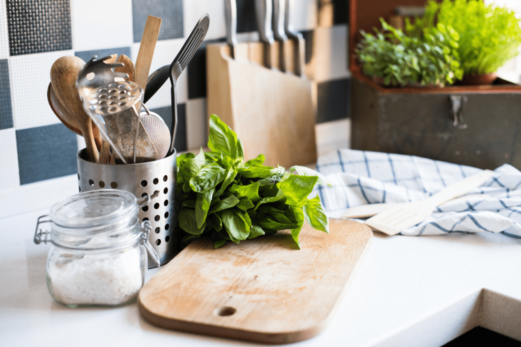 Kitchen counter with cutting board, flour, lettuce, a jar of utensils, knife block, hand towel, and plant